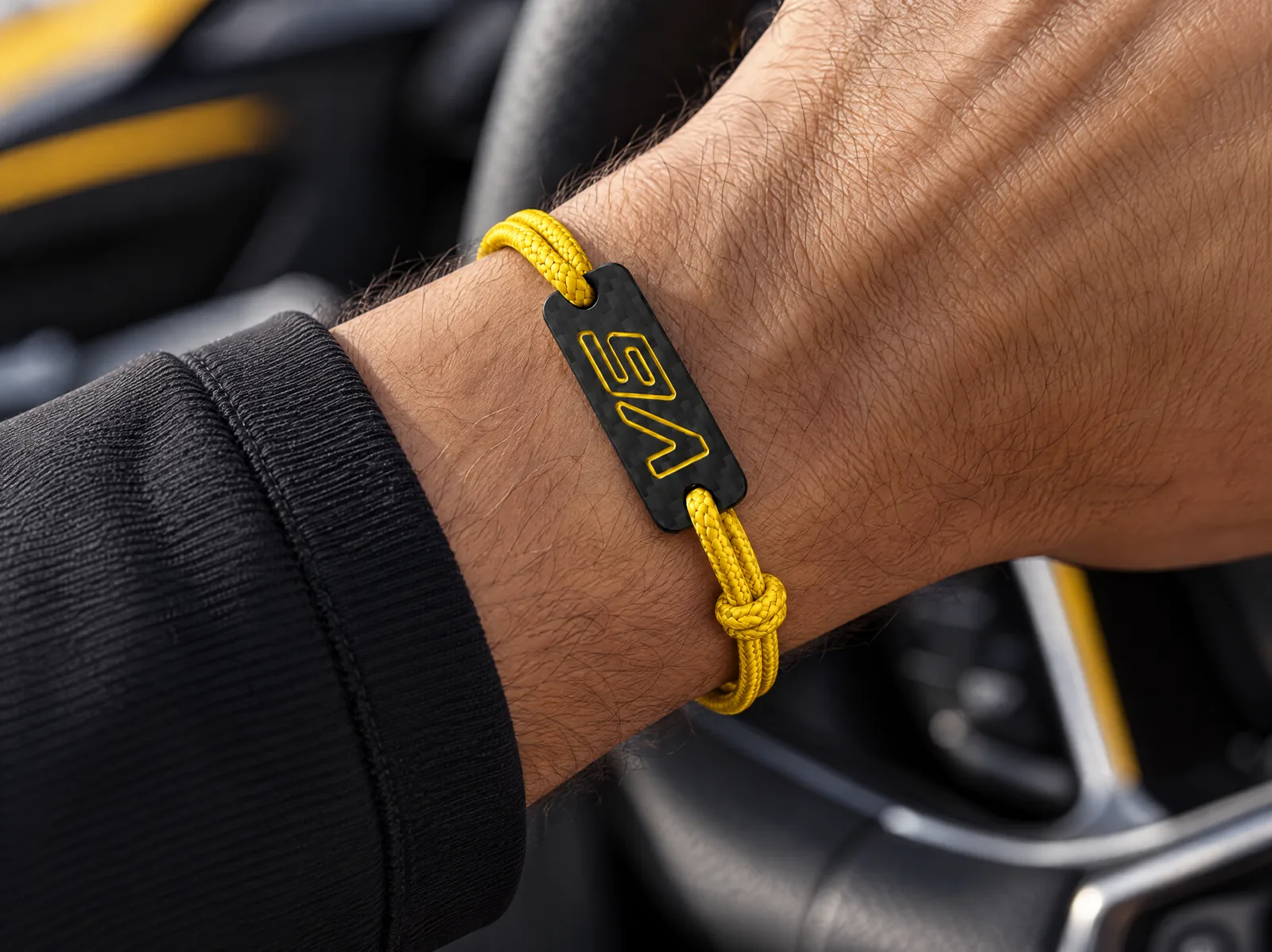 Bracelet V6 Carbone jaune au poignet, main sur le volant