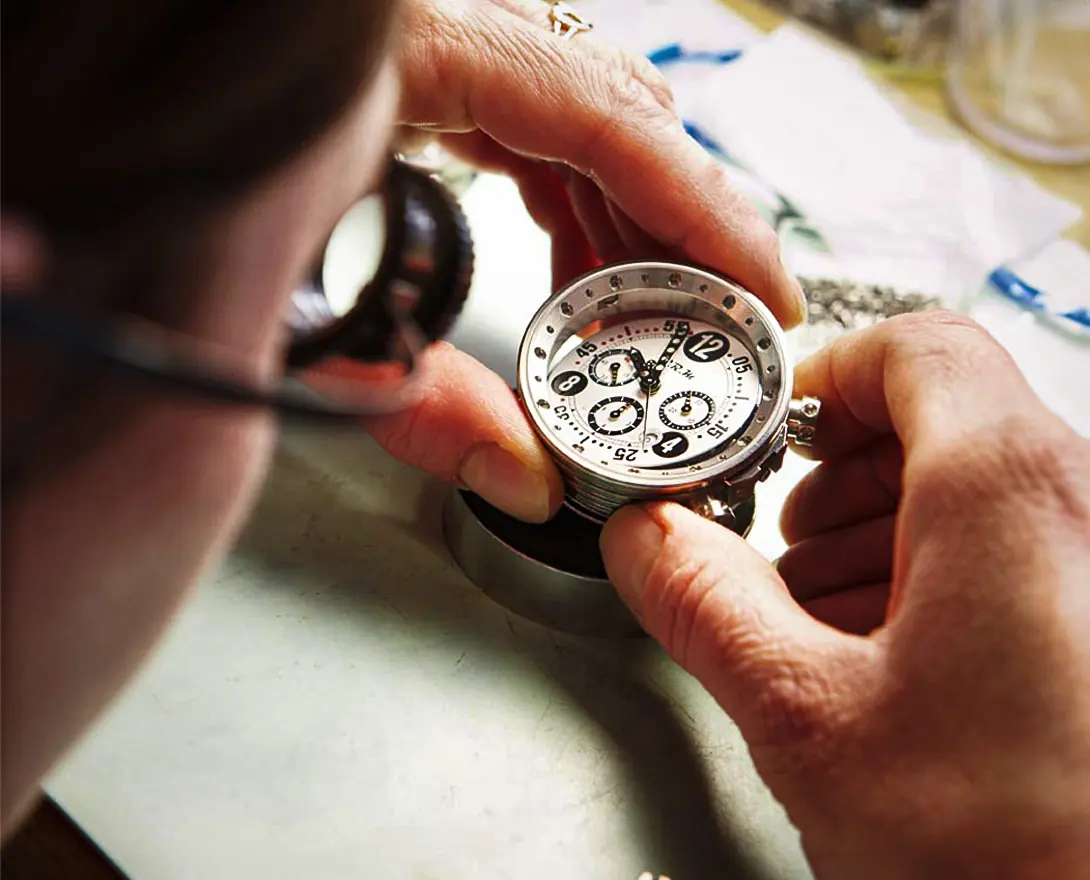 Un horloger, loupe à l'œil, examine un chronographe B.R.M à cadran blanc