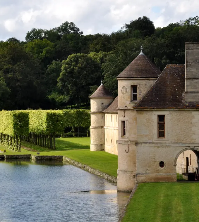 Un château aux tourelles, entouré d'eau et de jardins taillés, dans la campagne