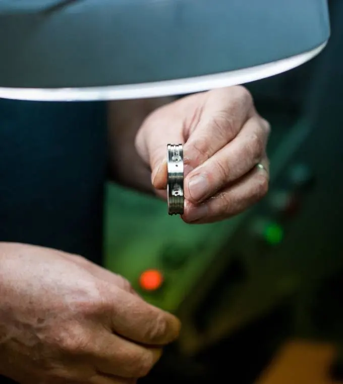 Sous la lampe de l'atelier, une main tient une petite pièce usinée