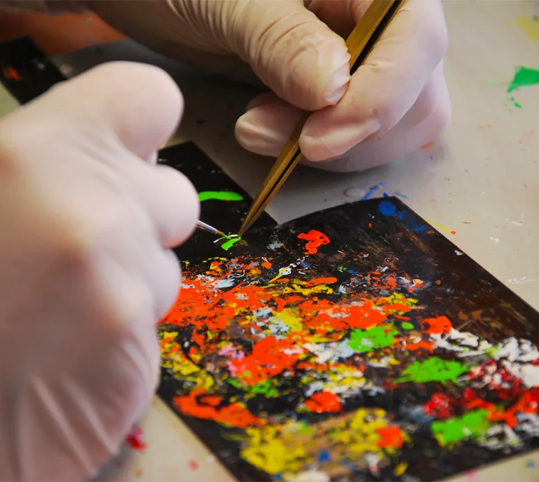 Main gantée déposant la laque au pinceau fin, sur une palette d'essais multicolore