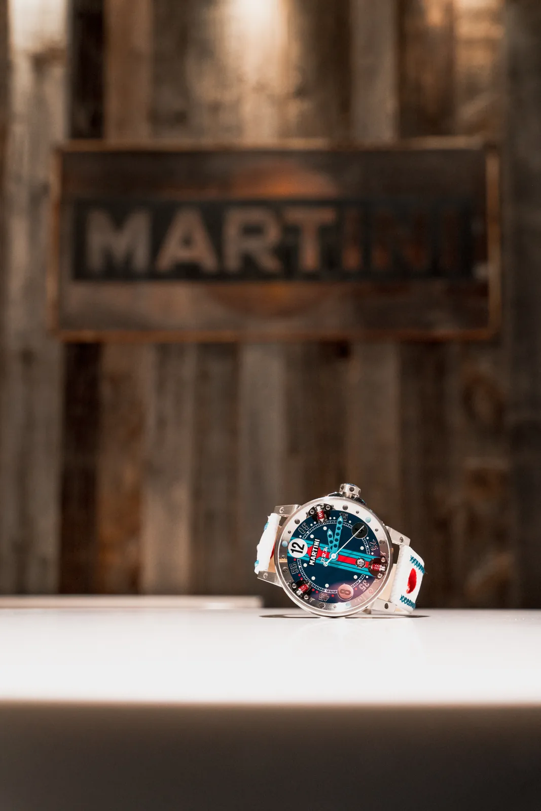 B.R.M Uhr mit Martini Racing Zifferblatt auf einem Tisch liegend, vor einem hölzernen Martini-Schild