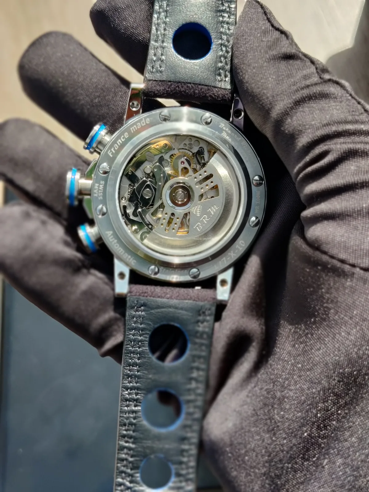 Fond saphir : masse ajourée B.R.M et mécanique du chronographe (Valjoux) dans la main gantée