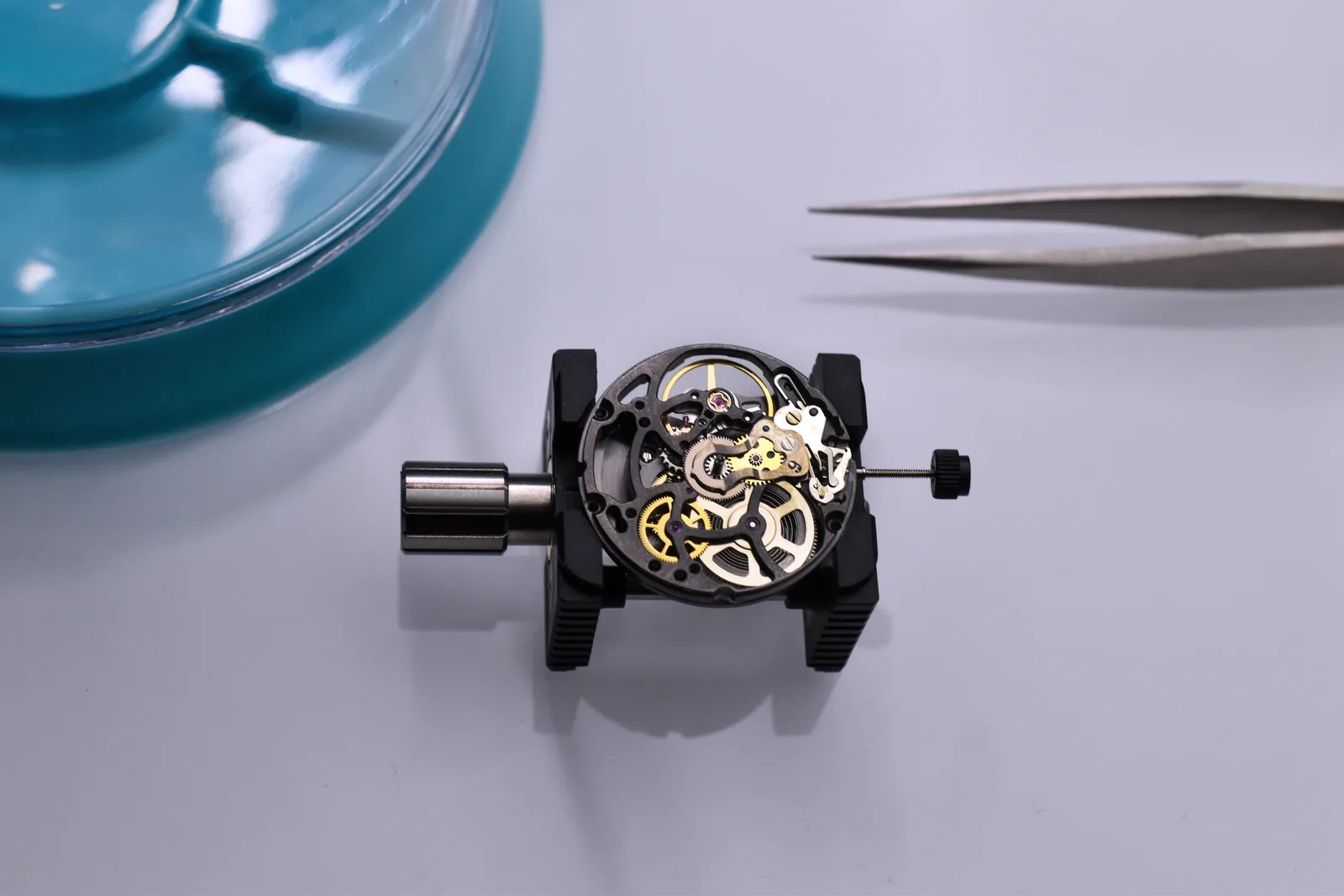 Mouvement chronographe squelette (PVD noir, roues dorées) sur son support d'horloger, brucelles